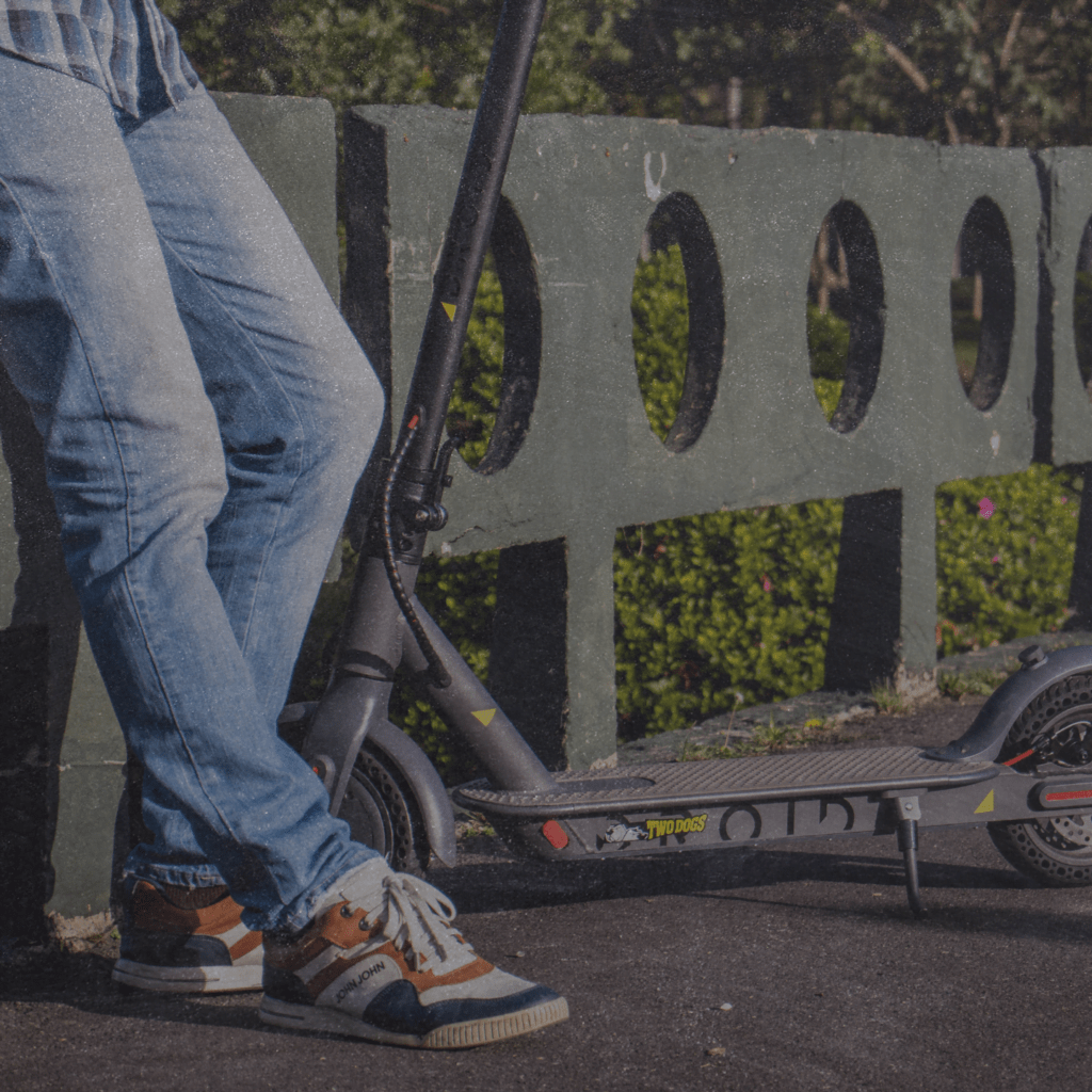 Pessoa encostada em uma ponte de cimento com seu patinete Droid ao lado.