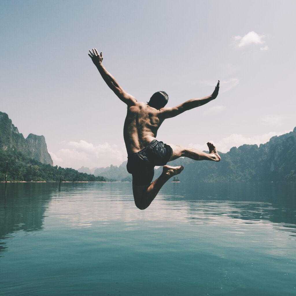 Homem pulando em um lago em um dia agradavél. 