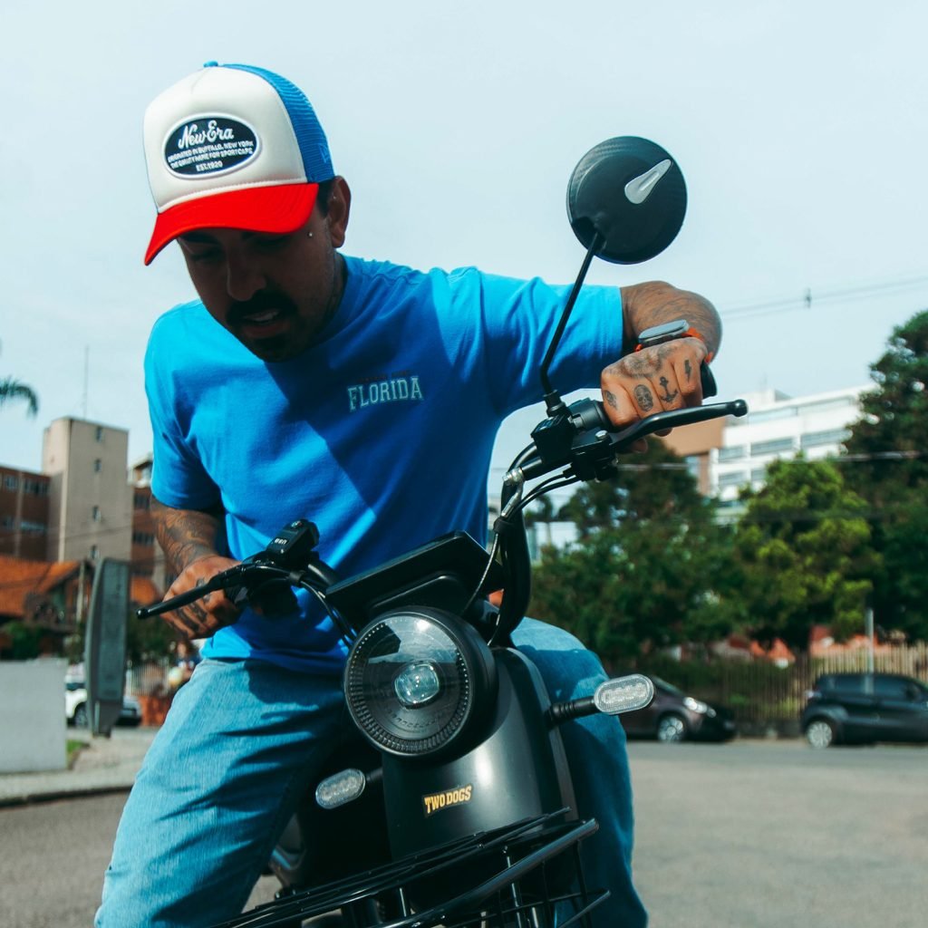 Homem de camiseta azul sentado em uma bicicleta elétrica preta da Two Dogs, em ambiente urbano. Imagem ilustrativa do artigo sobre quanto tempo dura a bateria de uma bicicleta elétrica.